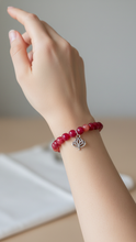 Load image into Gallery viewer, Hand wearing a Sasha L Jewels red beaded bracelet with a silver lotus charm on a neutral background