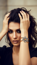 Load image into Gallery viewer, Woman wearing a Sasha L Jewels decorative beaded bracelet with a large stone and flower design, posing with hands on her hair.