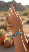 Load image into Gallery viewer, Hand model wearing Sasha L Jewels turquoise bracelet with arrow design against a desert background